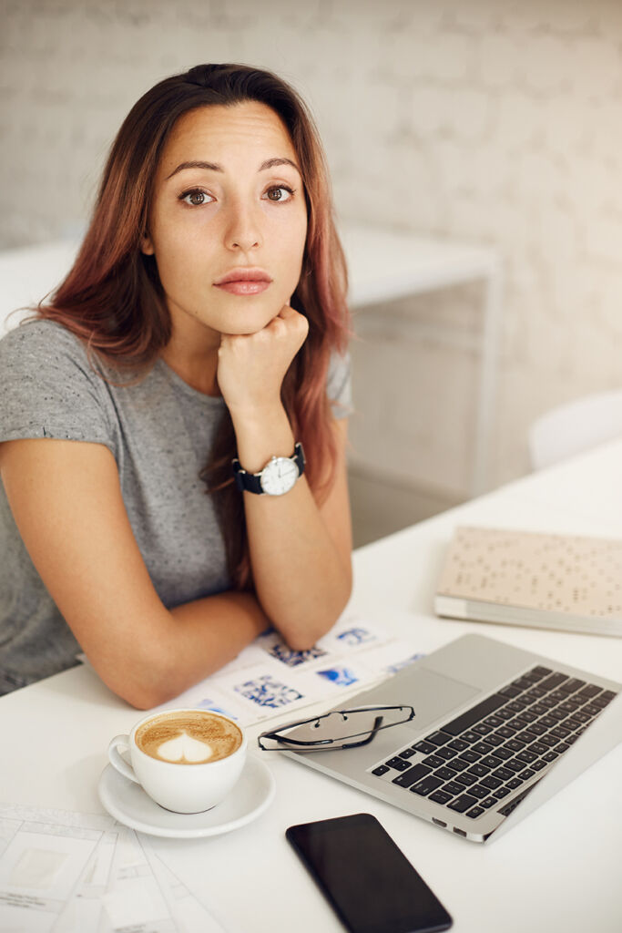 Woman looking at camera using laptop drinking coffee in cafe or coworking space or campus.