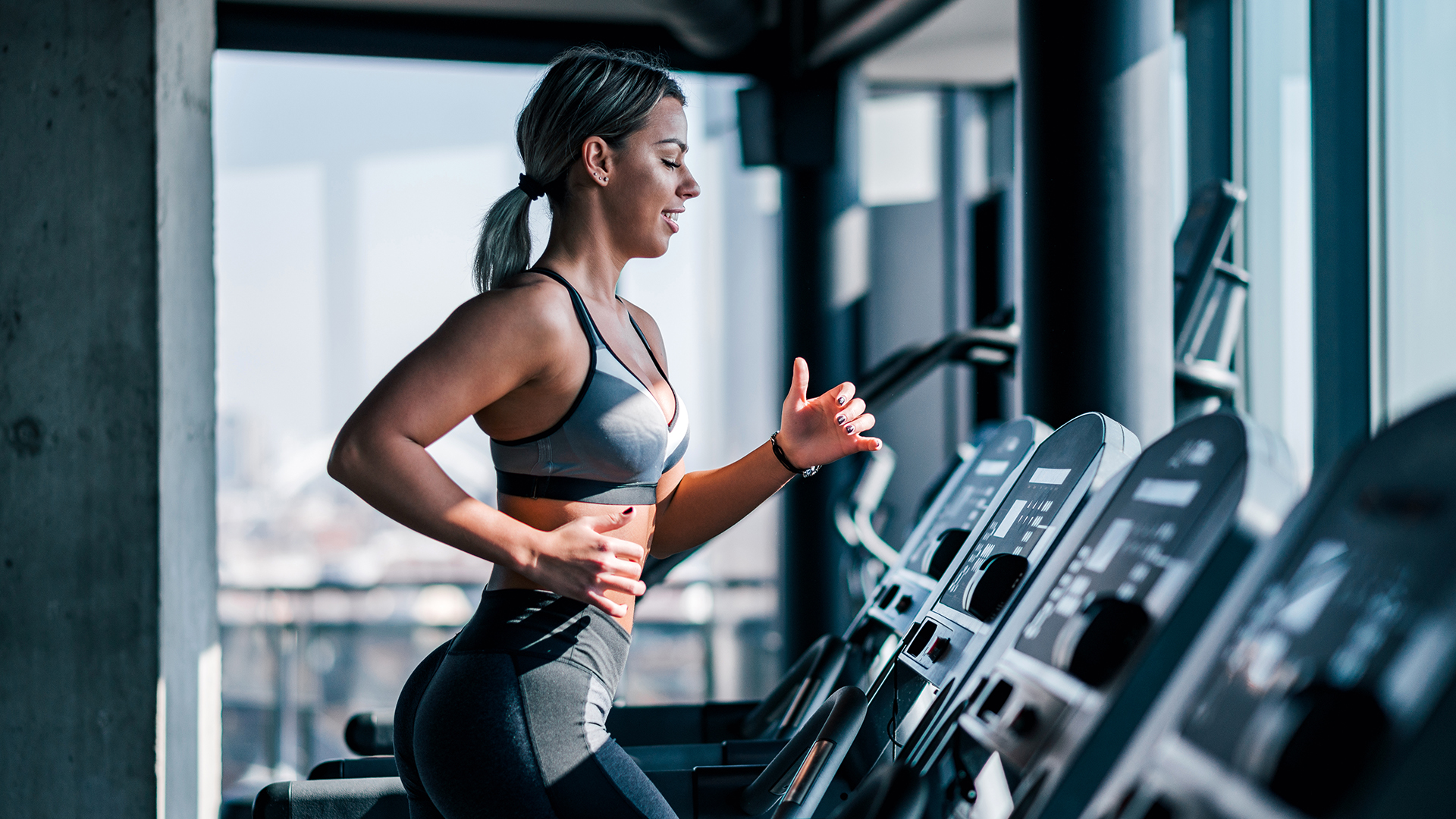 Side view of beautiful muscular woman running on treadmill.