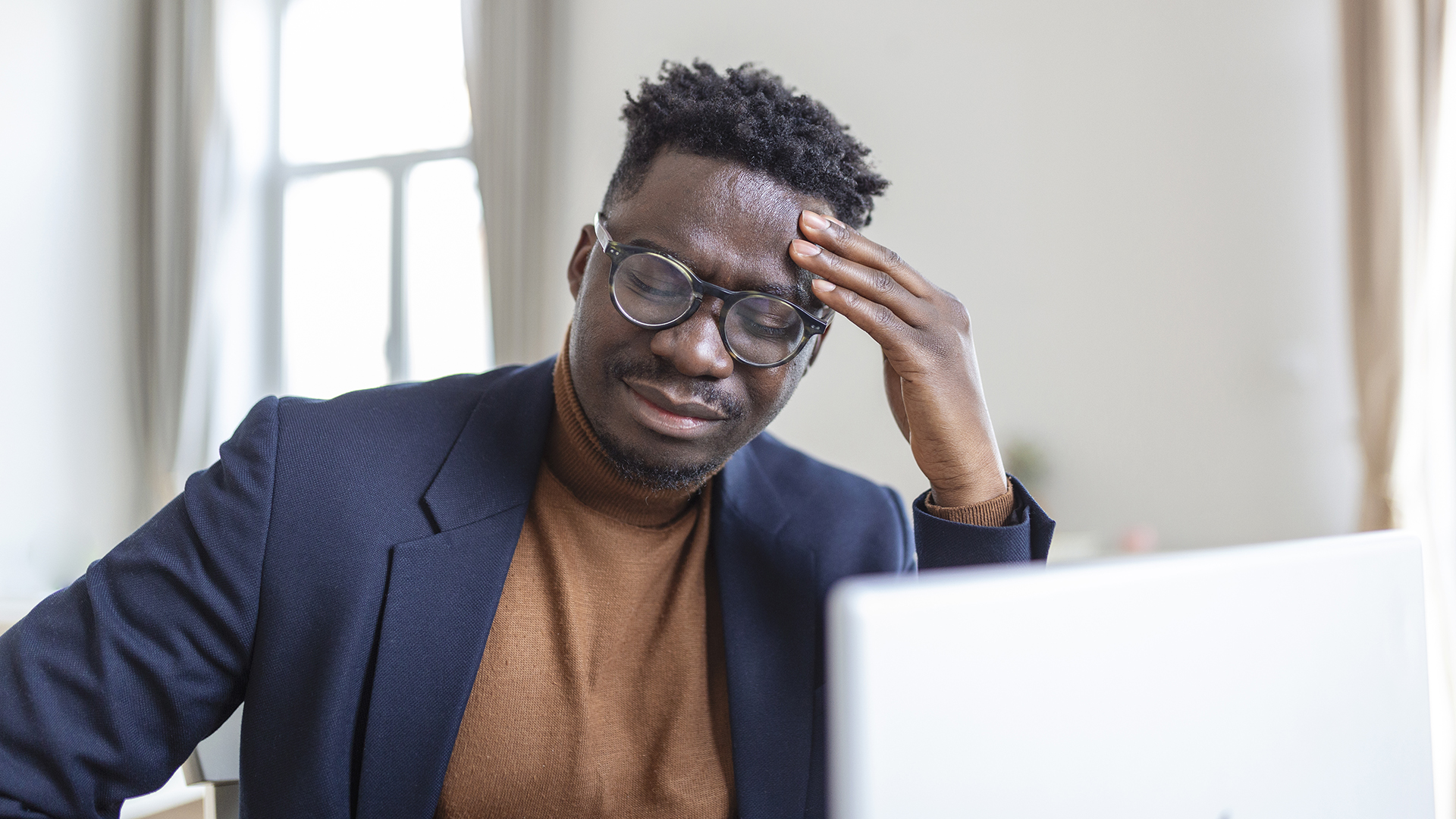Head shot stressed young african american man touching forehead, suffering from terrible headache, working on computer at home office. Frustrated confused biracial guy having painful feelings in head.